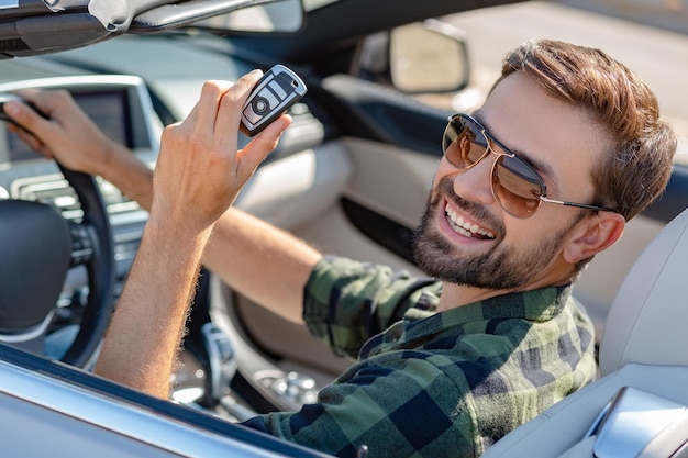 Portrait of happy man holding key of the convertible and looking at the camera