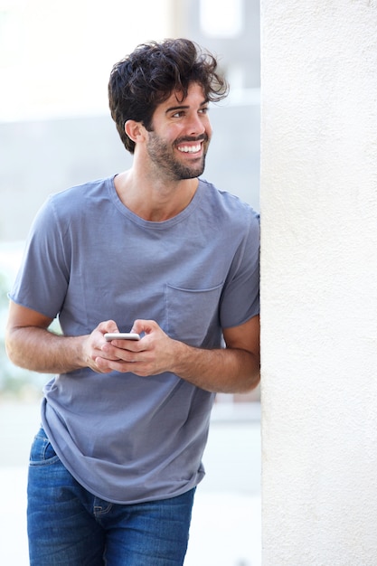 Portrait of happy man holding phone leaning on wall outside