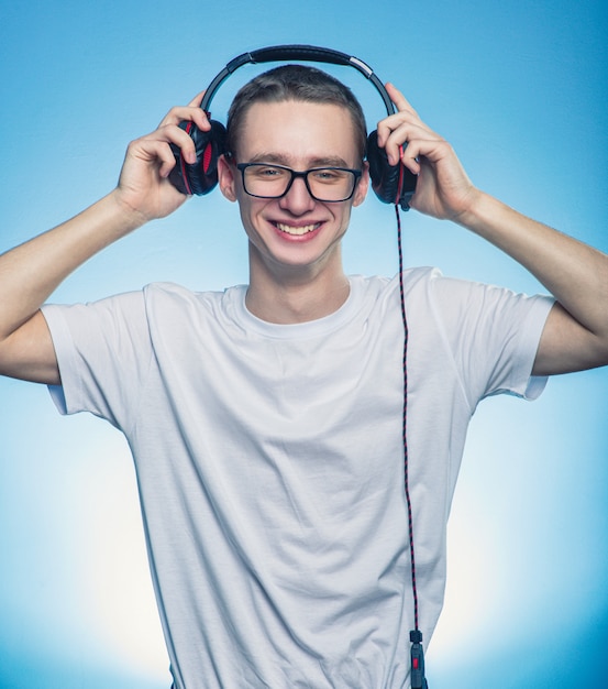 Portrait of a happy man listening the music in headphones and removed them from head over blue background.