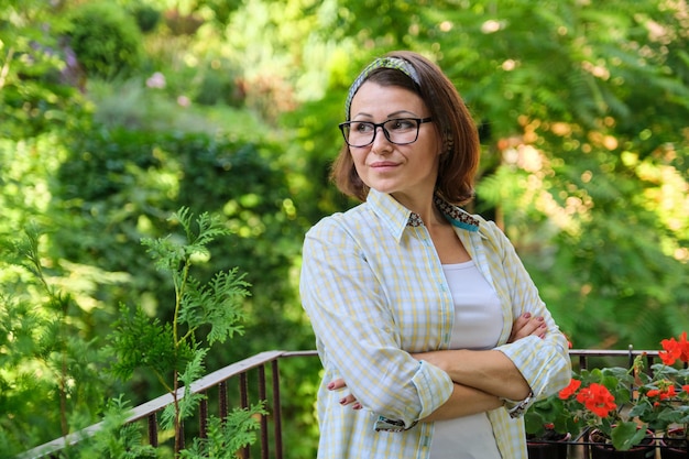 Portrait of happy middle-aged woman, confident smiling female with folded arms on home outdoor landscaped balcony