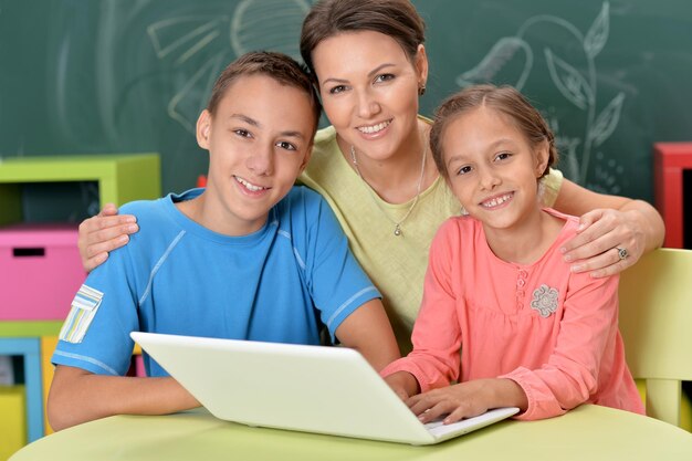 Portrait of happy mother and children sitting at table with laptop