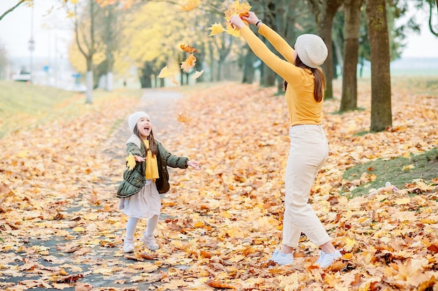 Portrait of happy mother and daughter in autumn forest at sunset. Young Mother and daughter walking in the autumn park. Autumn women.