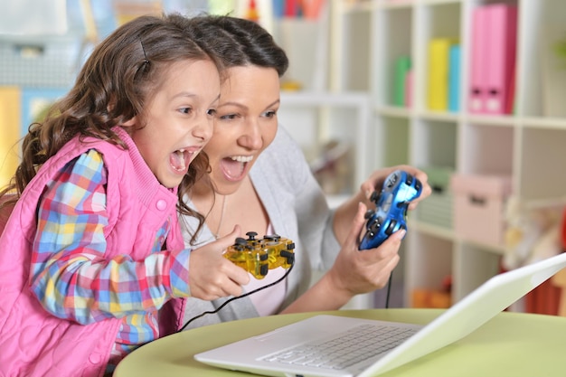 Portrait of happy mother and daughter playing game on laptop