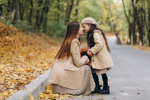 Portrait of happy mother and daughter spending time together in autumn park with falling yellow leaves