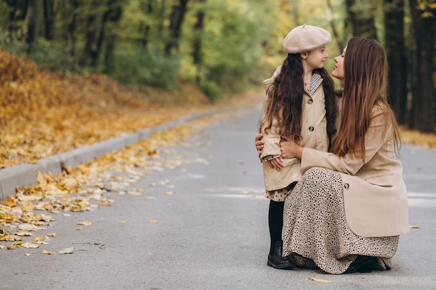 Portrait of happy mother and daughter spending time together in autumn park with falling yellow leaves