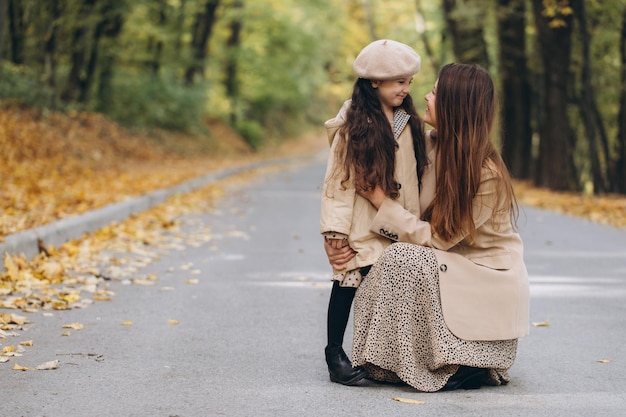 Portrait of happy mother and daughter spending time together in autumn park with falling yellow leaves