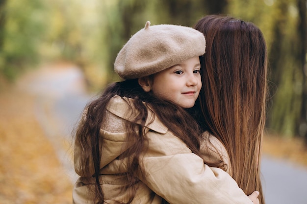 Portrait of happy mother and daughter spending time together in autumn park with falling yellow leaves