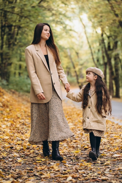 Portrait of happy mother and daughter spending time together in autumn park with falling yellow leaves