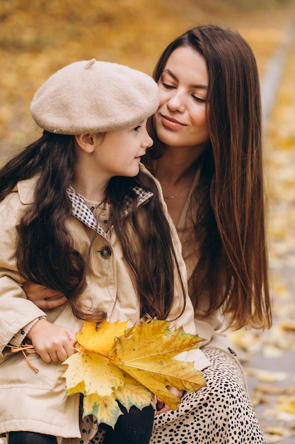 Portrait of happy mother and daughter spending time together in autumn park with falling yellow leaves