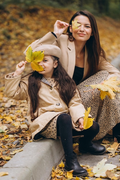 Portrait of happy mother and daughter spending time together in autumn park with falling yellow leaves