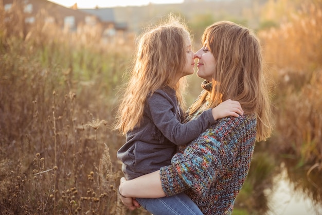 Portrait happy mother kissing child in warm sunny autumn day