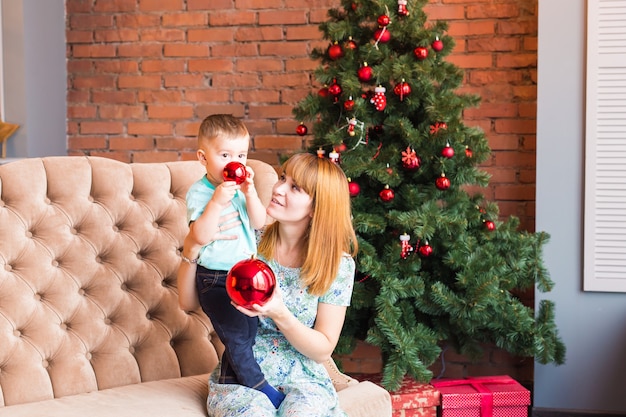 Portrait of happy mother and laughing baby holding bauble against domestic festive interior with