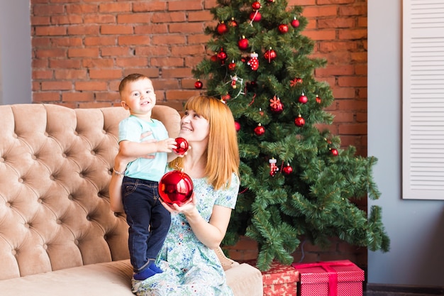 Portrait of happy mother and laughing baby holding bauble against domestic festive interior with