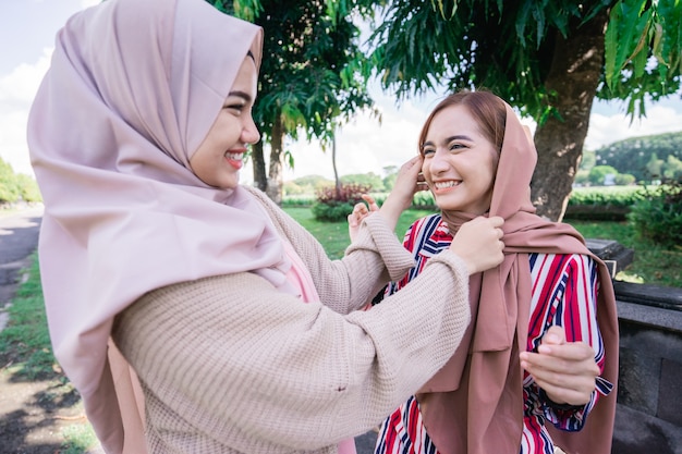 Portrait of happy muslim asian woman fixing friend hijab while meeting outdoor