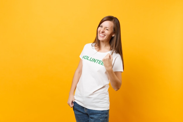 Portrait of happy overjoyed excited woman in white t-shirt with written inscription green title volunteer isolated on yellow background. Voluntary free assistance help, charity grace work concept.