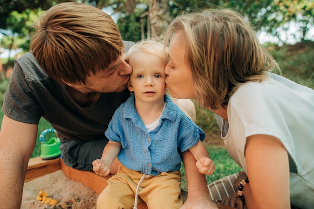 Portrait of happy parents kissing child in sandpit