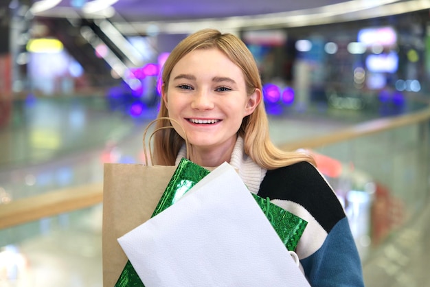 Photo portrait of happy positive stylish girl young teen teenager beautiful woman is smiling having fun in mall during shopping carrying holding shopping paper bags in hand