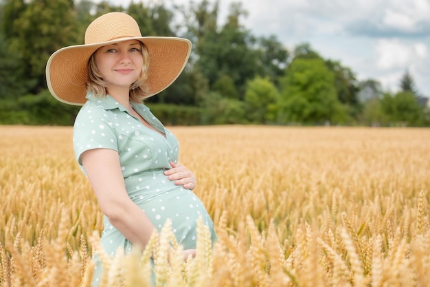 Portrait of happy pregnant woman in hat in field of golden wheat or barley Expectant mother