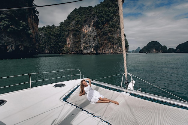 Portrait of happy pretty girl with white dress and long curly blonde hair lying on yacht at summertime. looking at camera with toothy smile.