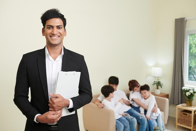 Portrait of happy real estate agent with documents standing in house he sold to family with two children