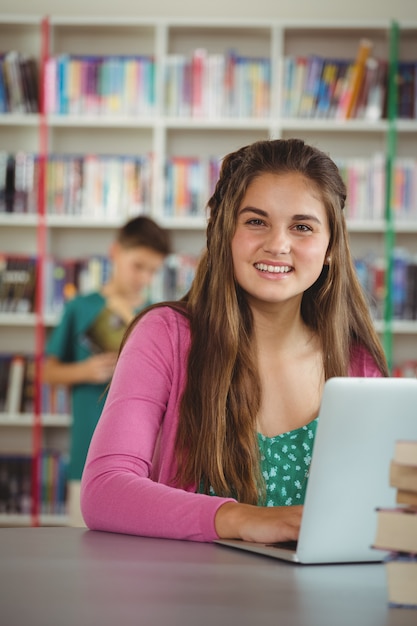 Portrait of happy schoolgirl using laptop in library