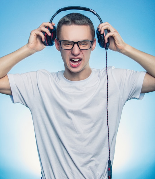 Portrait of a happy screaming man listening music in headphones and removed them from head over blue background.