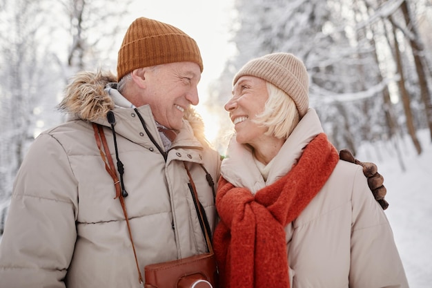 Portrait of happy senior couple enjoying walk in winter forest and looking at each other