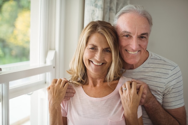 Portrait of happy senior couple standing next to window