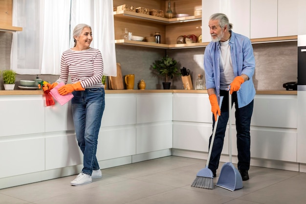 Portrait Of Happy Senior Spouses Making Cleaning In Kitchen Together