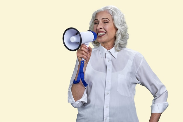 Portrait of happy senior woman with megaphone isolated on yellow