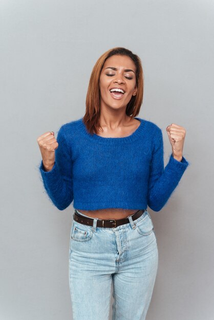 Portrait of happy smiling african woman in sweater and jeans with eyes closed.