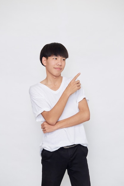 Portrait of a happy smiling Asian man wearing casual white t-shirt pointing hand to empty space beside on white background