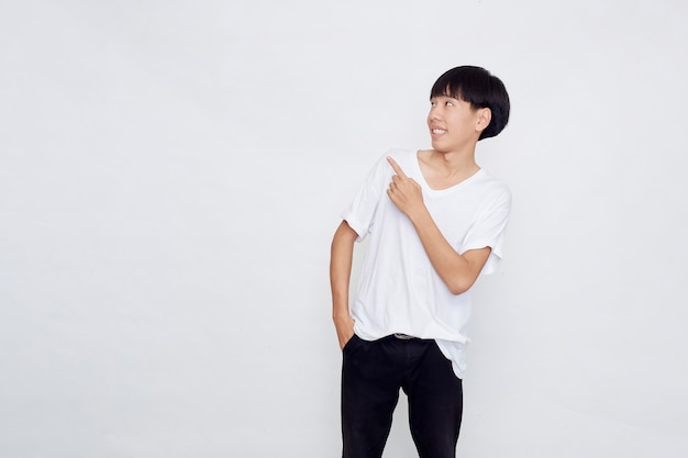 Portrait of a happy smiling Asian man wearing casual white t-shirt pointing hand to empty space beside on white background