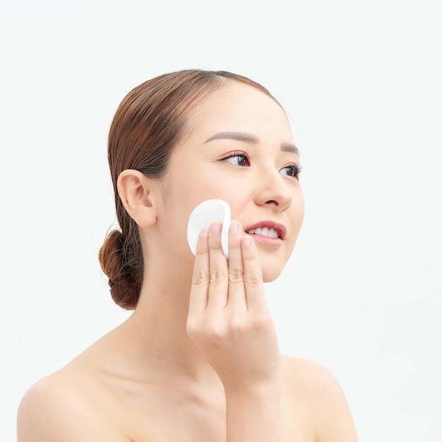 Portrait of happy smiling beautiful young woman cleaning skin by cotton pad over white background