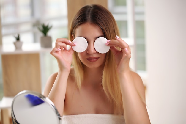 Portrait of happy smiling beautiful young woman cleaning skin with cotton swab, at home.