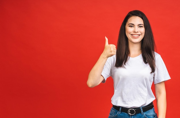 Portrait of happy smiling brunette business girl woman in casual isolated over red background Thumbs up