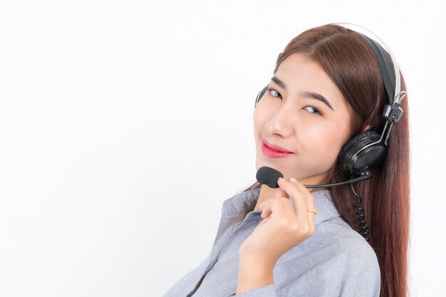 Portrait of happy smiling female customer support phone operator wearing a white shirt with headset holding the earphone isolated on white