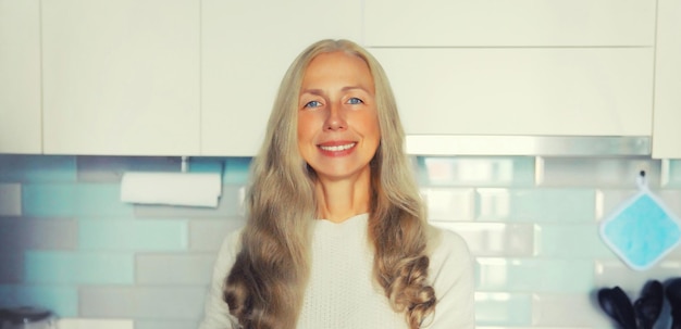 Photo portrait of happy smiling middle aged woman housewife in the kitchen at home looking at camera