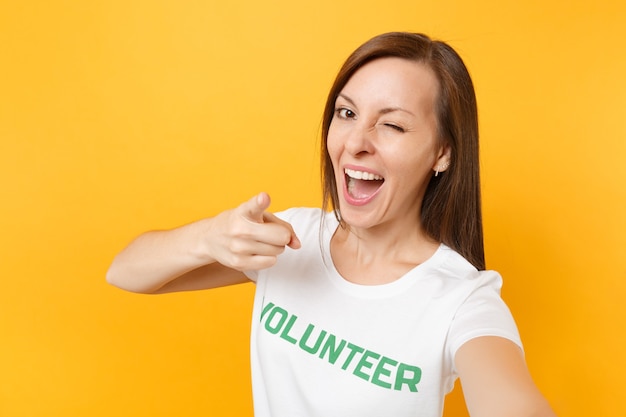 Portrait of happy smiling satisfied woman in white t-shirt with written inscription green title volunteer isolated on yellow background. Voluntary free assistance help, charity grace work concept.