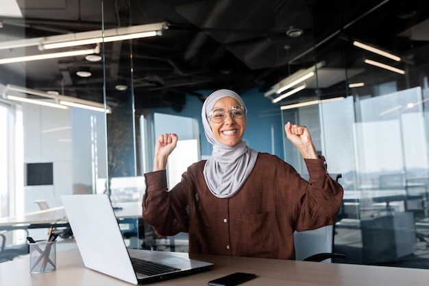 Portrait of happy smiling and successful muslim at work in office businesswoman with laptop holding