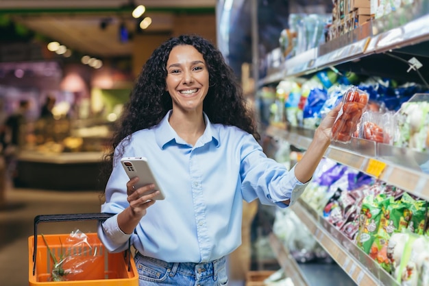 Portrait happy and smiling woman shopper in a supermarket hispanic using a smartphone to view a