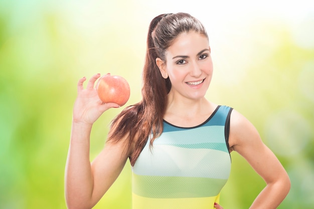 Portrait of happy smiling young beautiful woman in fitness wear with apple