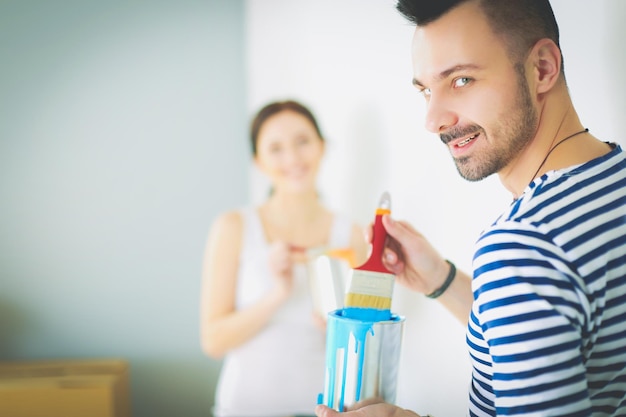 Portrait of happy smiling young couple painting interior wall of new house young couple