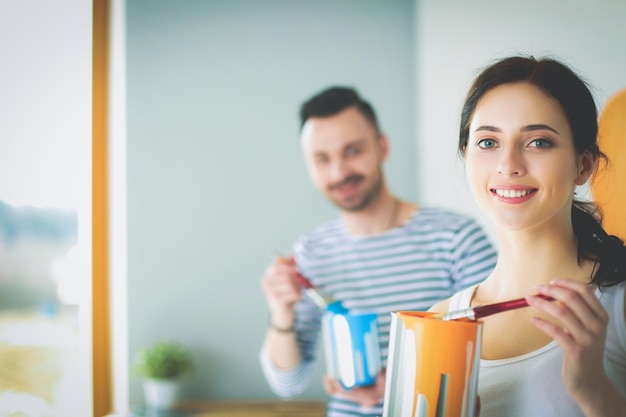 Portrait of happy smiling young couple painting interior wall of new house young couple