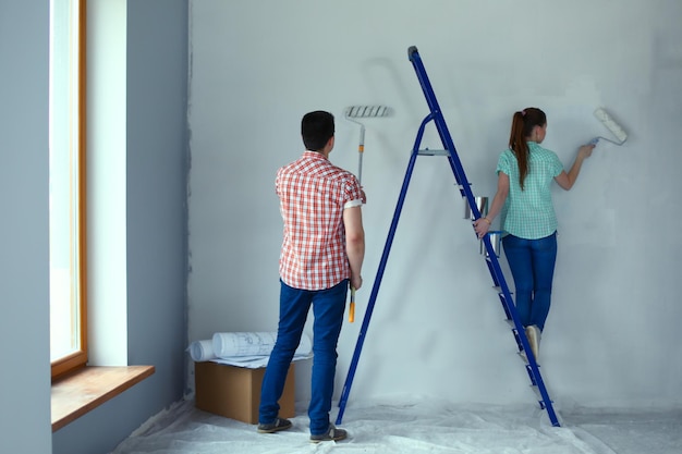 Portrait happy smiling young couple painting interior wall of new house Young couple