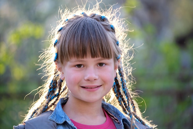 Portrait of happy smiling young teen girl in casual clothes with blue ribbons in long braids outdoors on summer or spring day