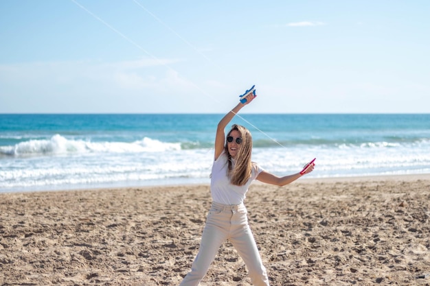 Portrait of happy smiling young woman flying a kite on the beach