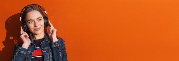 Portrait happy smiling young woman with headphones listening to music on orange