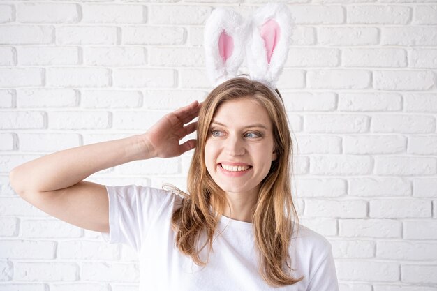 Portrait of a happy woman in bunny ears on white brick wall background