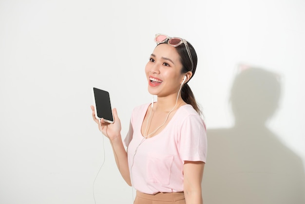 Portrait of a happy woman listening music in headphones and dancing isolated on a white background